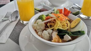 A dining table with a bowl of noodle soup, a glass of orange juice, and a plate of vegetables. - King Park Hotel Kota Kinabalu (Kota Kinabalu)