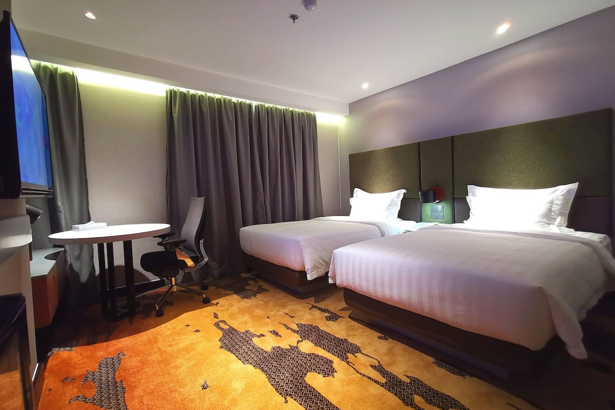 Habitación de hotel con dos camas, un escritorio, una silla y un televisor.