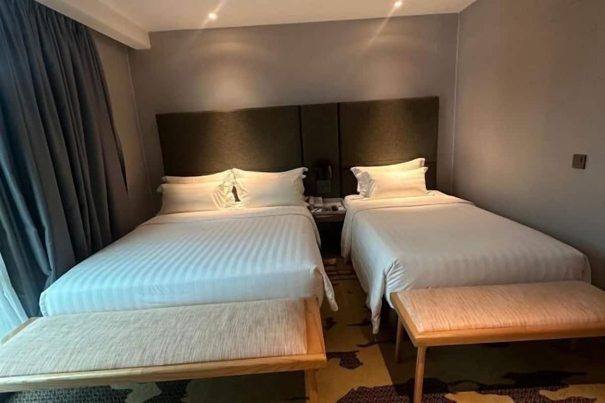 Una habitación de hotel con dos camas, un banco, una mesita de noche y un cabecero.