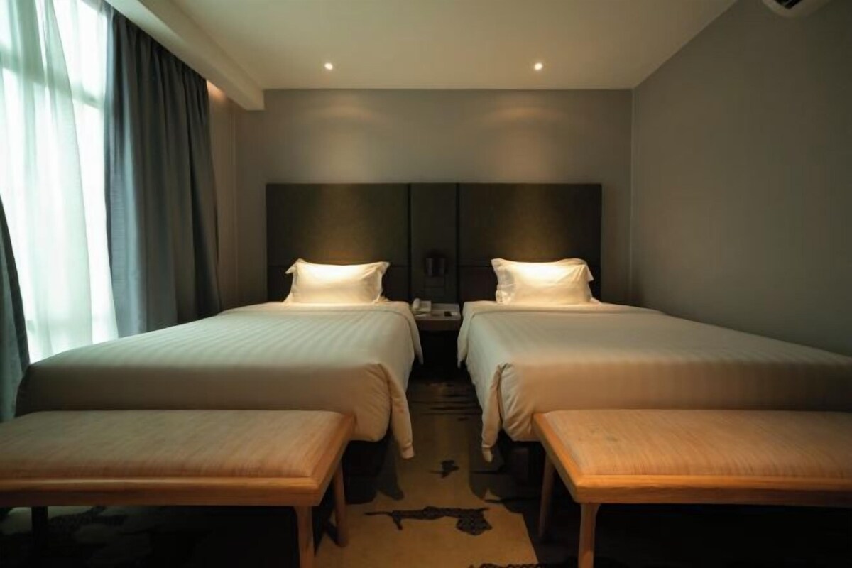 A hotel room with two beds, a bench, and a large window with curtains.