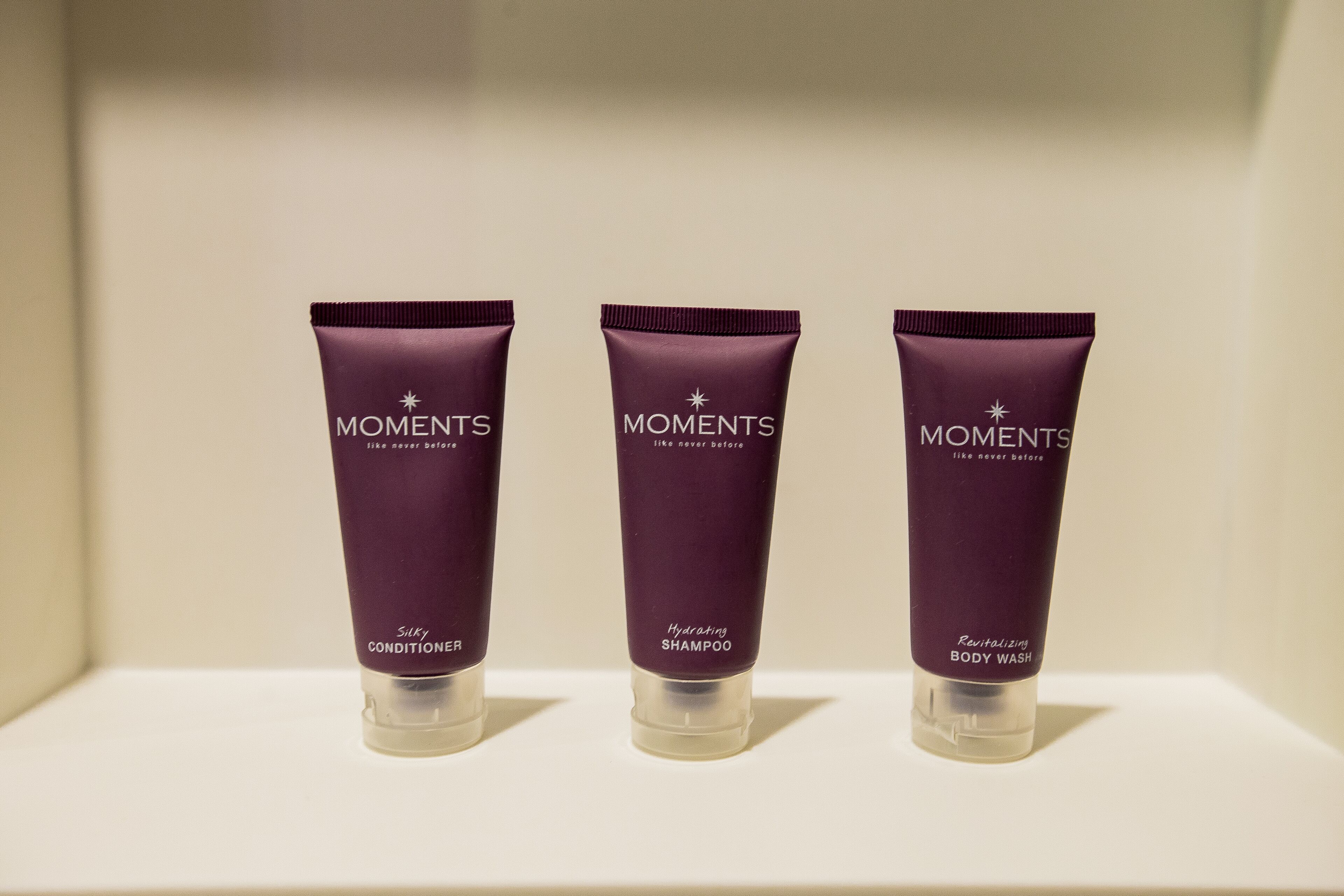 Three tubes of Moments body wash on a white shelf.