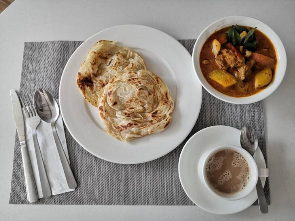 A plate of flatbreads, a bowl of curry, and a cup of coffee on a table.