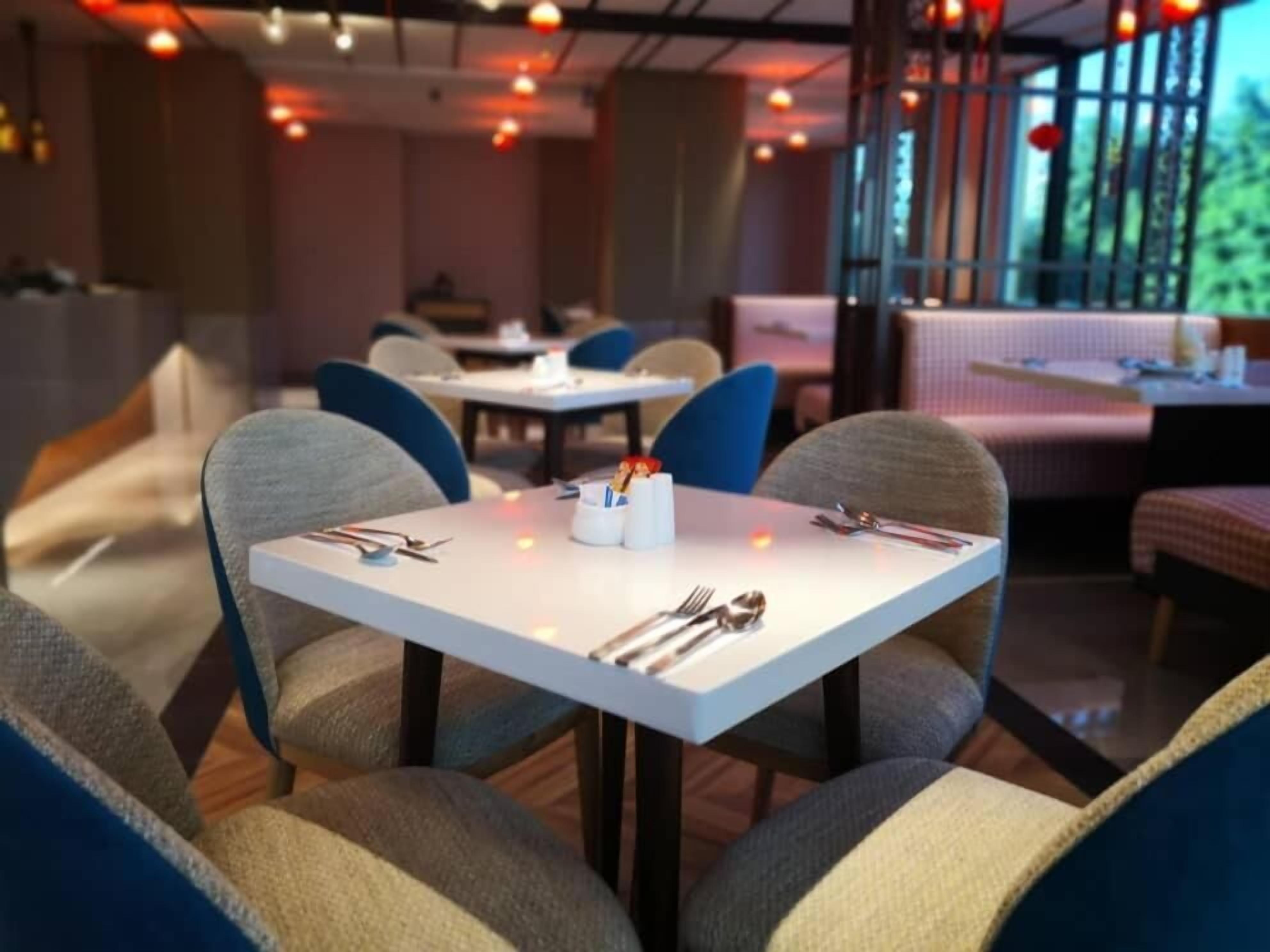 Un interior de restaurante con mesas cuadradas, sillas azules y vistas a zonas verdes.