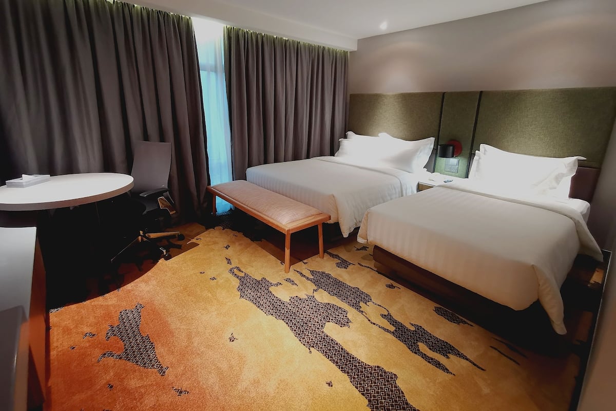 Habitación de hotel con dos camas, una mesa redonda, un banco y una alfombra estampada.