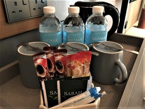 A breakfast setup with MOMA water bottles, a coffee maker, a mug, and a basket containing a Sabah coffee package and sugar packets. - King Park Hotel Kota Kinabalu (Kota Kinabalu)