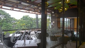 Een café met terras, een glazen wand en uitzicht op bomen.