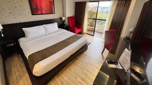 Een hotelkamer met een groot bed, een aan de muur bevestigde televisie, een rode stoel en een balkon met uitzicht.