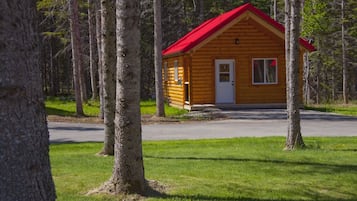 Una cabaña de troncos con techo rojo, rodeada de árboles y un espacio cubierto de césped.