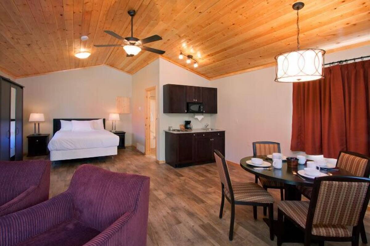 Quarto com cama, escrivaninha, mesa de jantar com cadeiras e ventilador de teto.