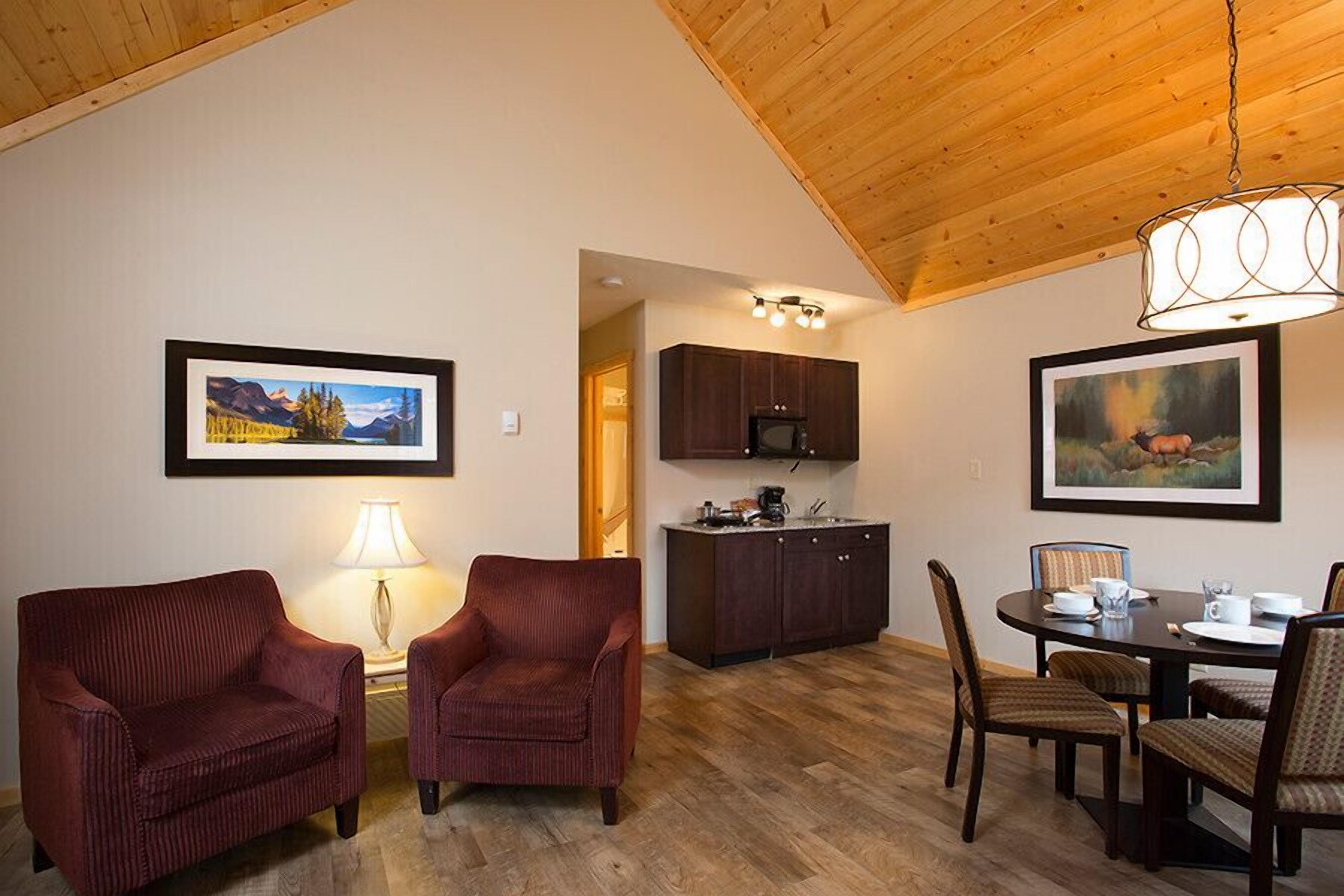 A dining area with a wooden ceiling, a table set for four, and two armchairs.