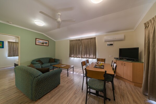 A living room with a sofa, a dining table, chairs, a TV, and an air conditioning unit.
