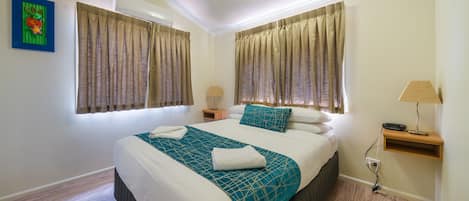 A neatly arranged bedroom with a large bed, two bedside tables, a nightstand, and a lamp.