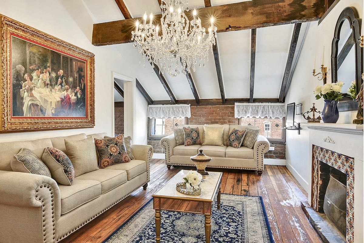 A spacious living room with a high ceiling, exposed beams, a chandelier, and a fireplace.