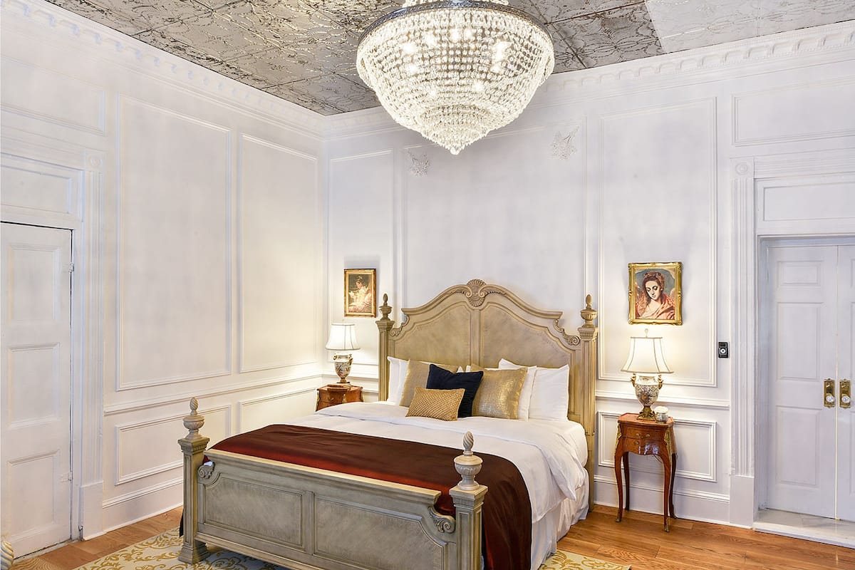 A classic bedroom with a large bed, ornate headboard, and a chandelier.