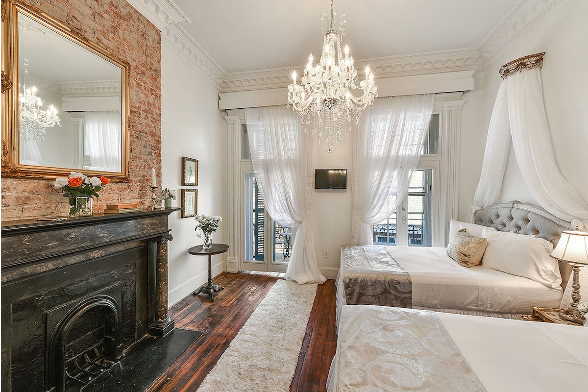 A bedroom with a fireplace, a chandelier, a bed, and a large mirror.