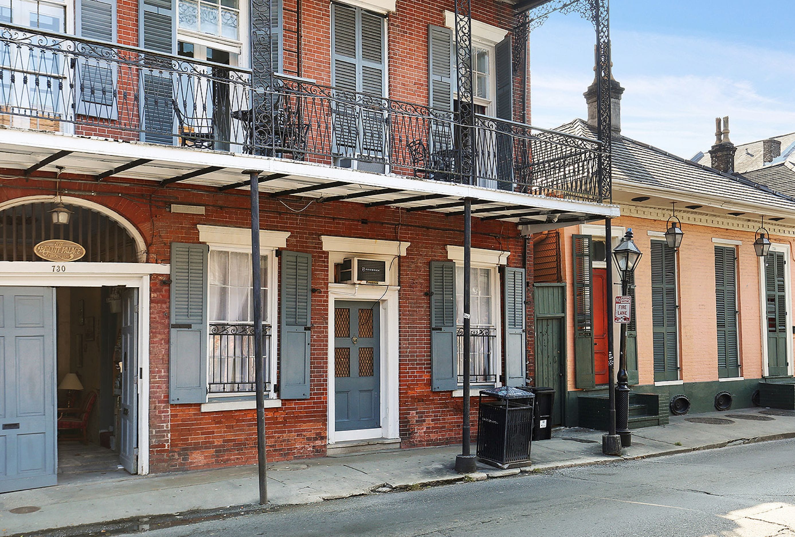 A row of brick buildings with green shutters, a balcony with wrought iron railings, and a street lamp.