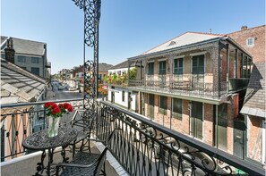 Een balkon met sierijzeren hekwerk, een tafel met een bloemenvaas, en uitzicht op een straat met gebouwen.