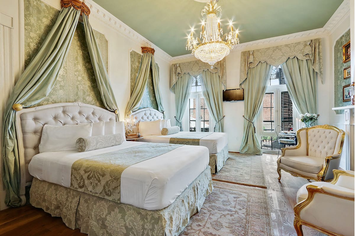 A luxurious bedroom with a large bed, two smaller beds, a chandelier, and classic decor.