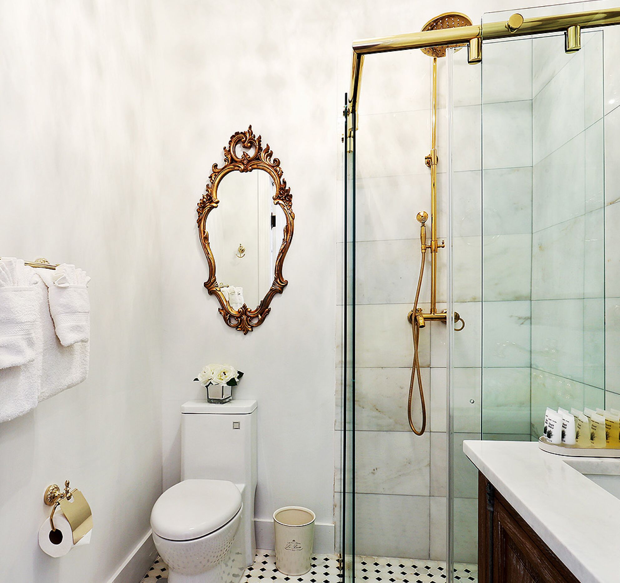 A bathroom with a toilet, a sink, a shower, and a decorative mirror.
