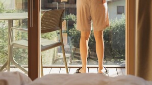 A woman standing by a sliding glass door, holding a child, with a view of a mountainous landscape and buildings in the background. - Hotel Mari Pop (Ried im Zillertal)