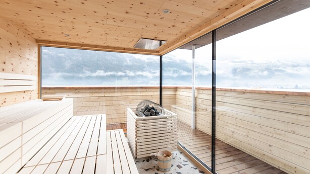 A wooden sauna with a large window, wooden benches, and a sauna heater. - Hotel Mari Pop (Ried im Zillertal)