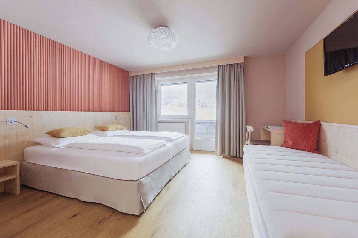 Una habitación de hotel con una cama grande, una cama más pequeña, un escritorio y una ventana con cortinas.
