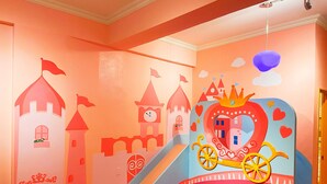 Una habitación infantil con un mural de un castillo, un tobogán y una cama con cabecera en forma de corazón.
