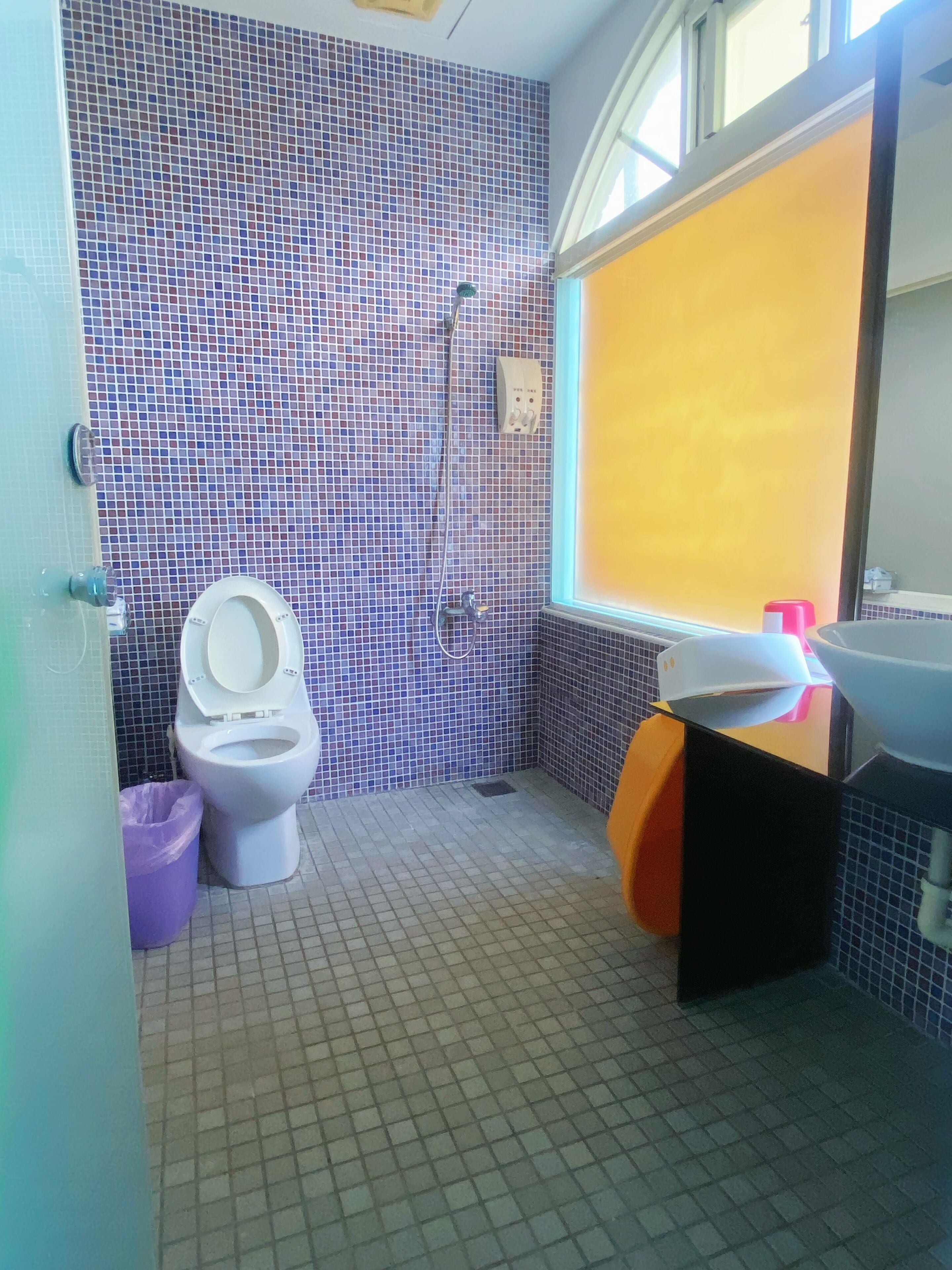 Un baño con pared de azulejos, un inodoro, un lavamanos y una ventana.