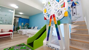 Zona de juegos infantiles con un tobogán, una noria de colores y un mural con un castillo.