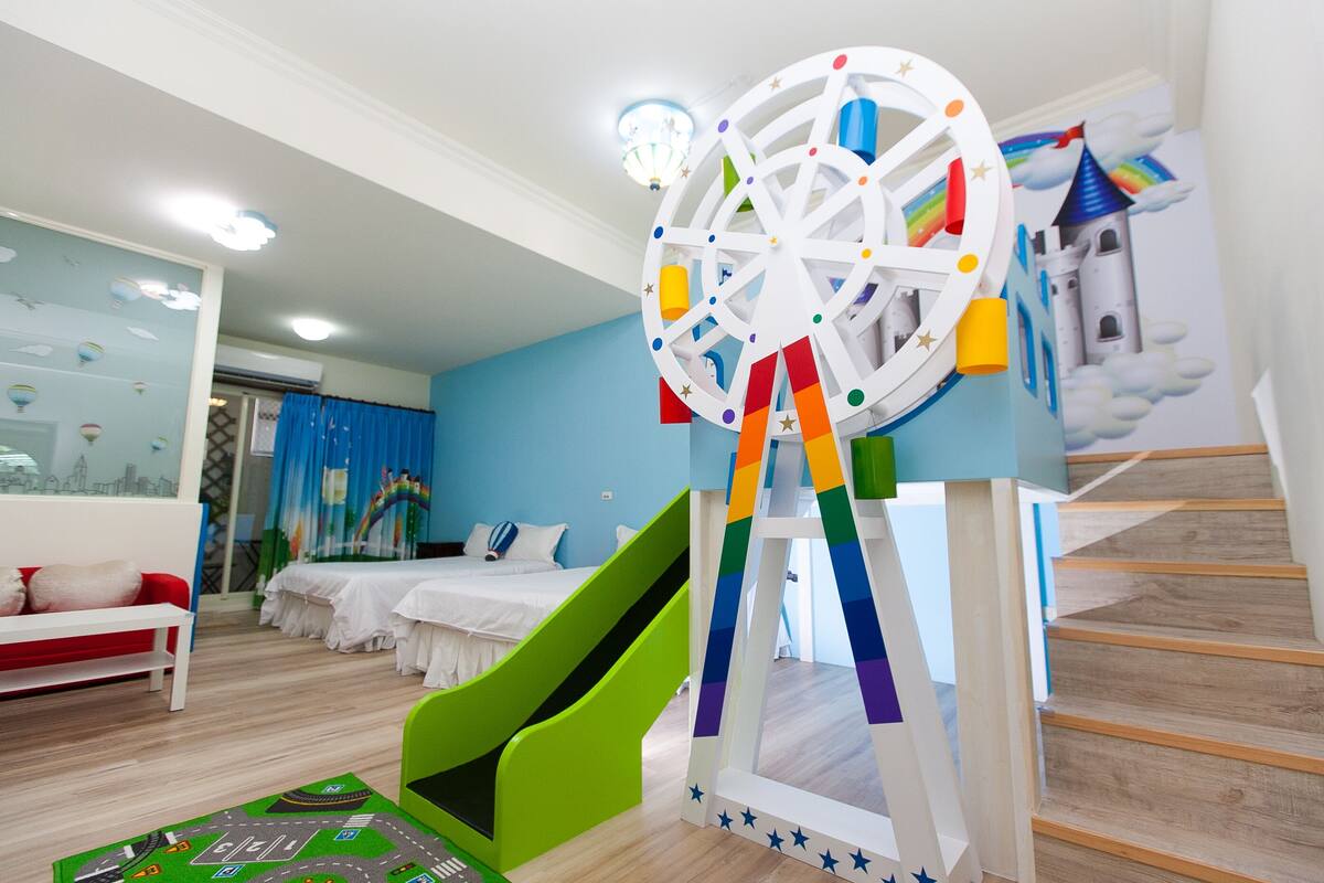 A children's play area with a slide, a colorful spinning wheel, and a mural of a castle.