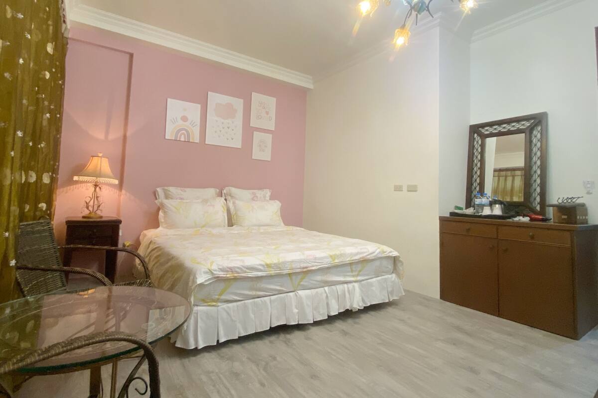 A bedroom with a bed, a nightstand, a chair, a dresser, and a mirror.