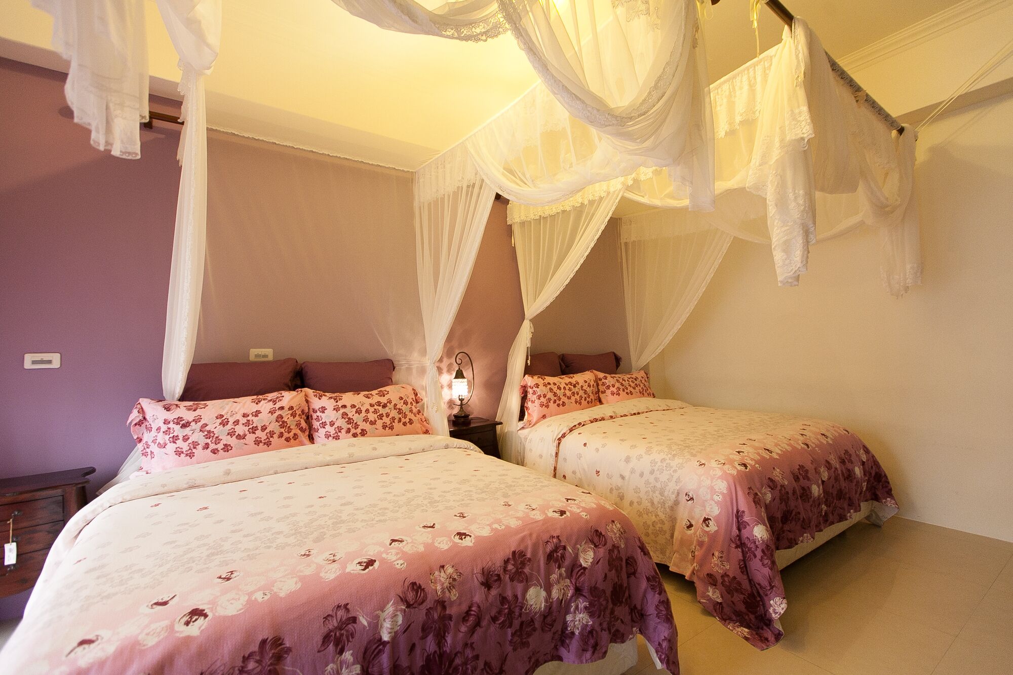 Un dormitorio con dos camas, cada una con ropa de cama floral, una mesita de noche y una lámpara de noche.
