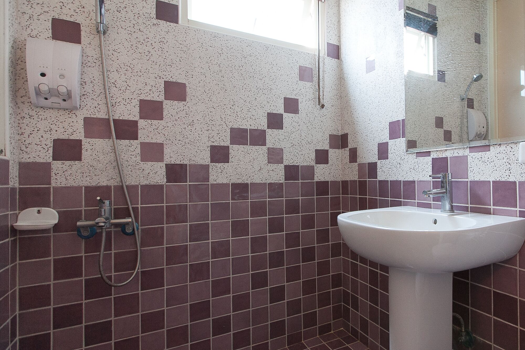 A bathroom with a white sink, a handheld showerhead, and a tiled wall with a pattern of purple and white squares.