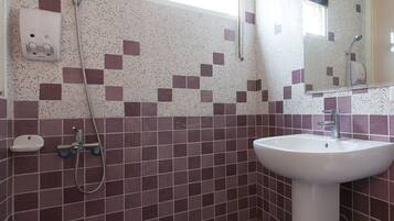 A bathroom with a white sink, a handheld showerhead, and a tiled wall with a pattern of purple and white squares.
