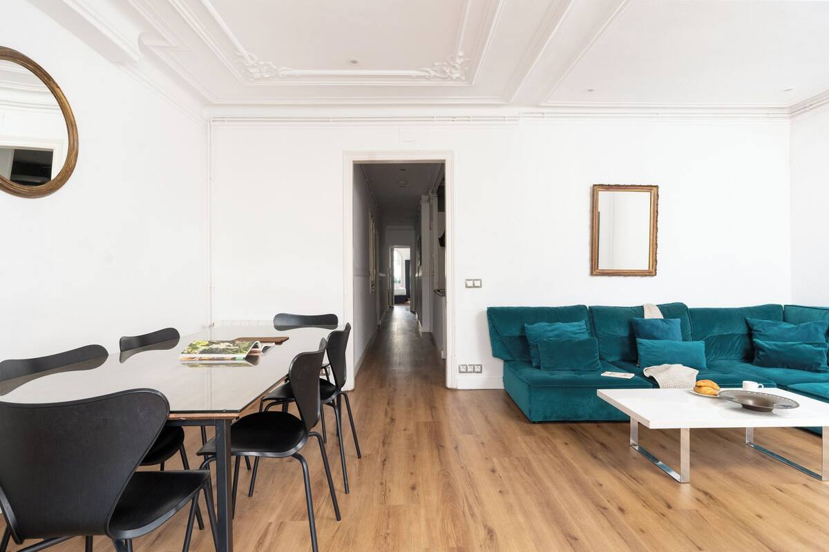 A modern living room with a dining area, teal sofa, and a white table.