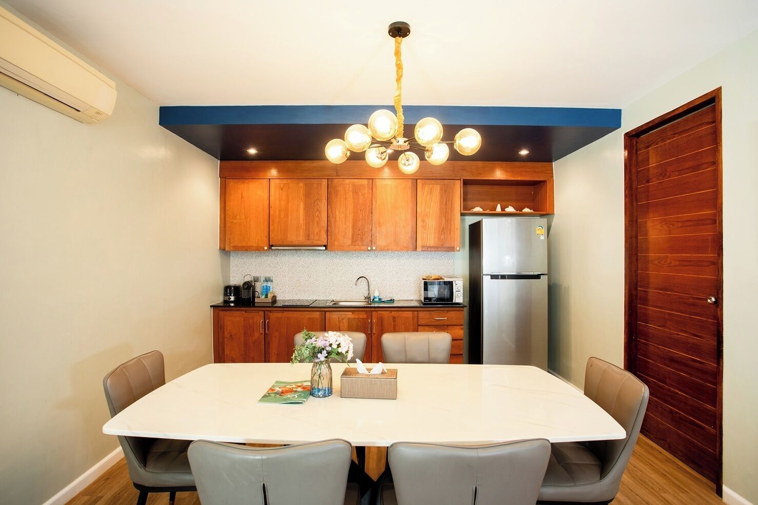 Una cocina compacta con armarios de madera, un refrigerador de acero inoxidable y una mesa de comedor con cuatro sillas.