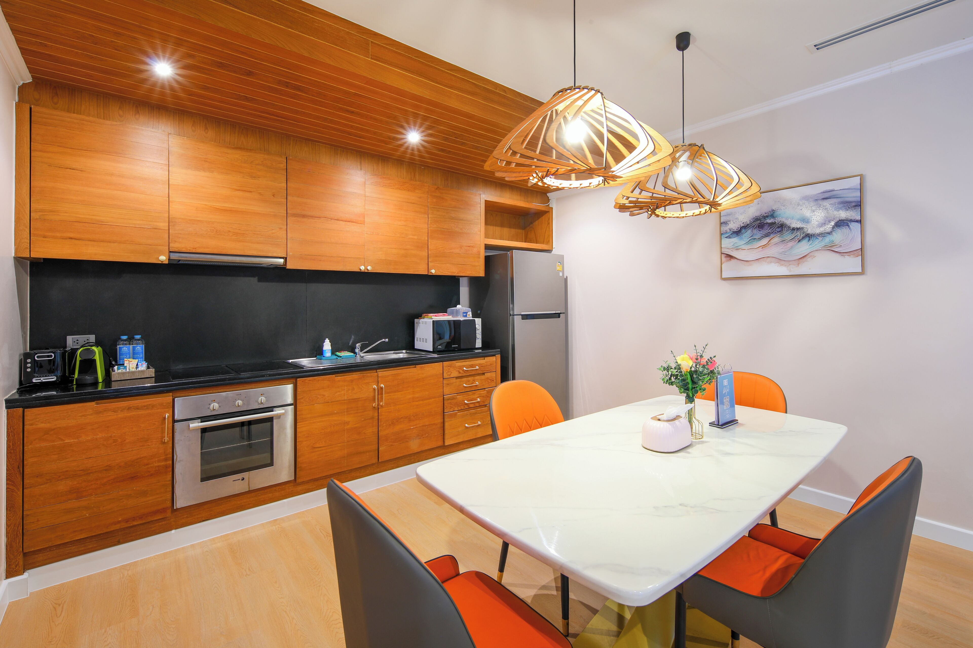 A modern kitchen with wooden cabinets, a stainless steel oven, and a dining area with a marble table and orange chairs.