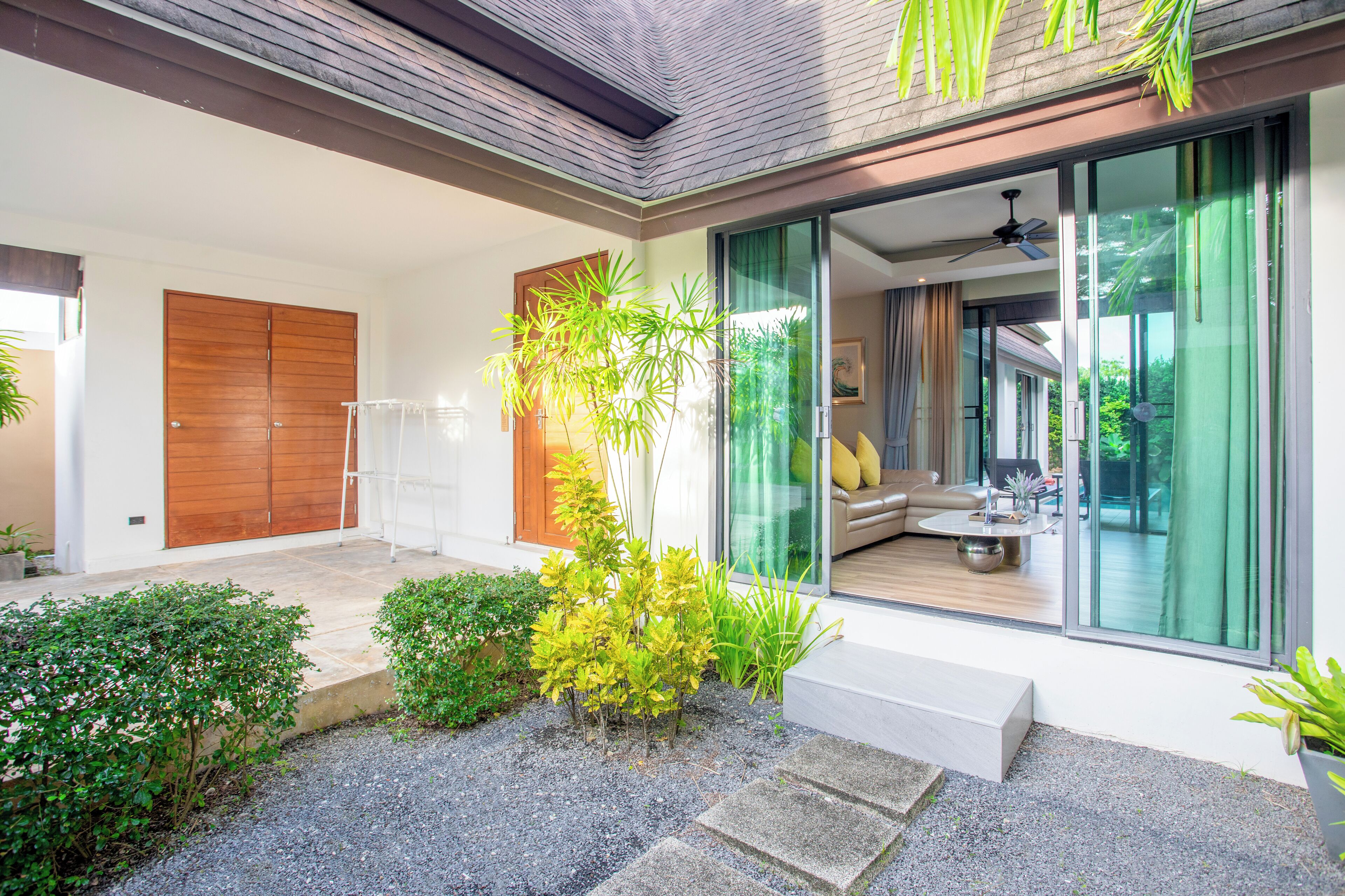 Een modern huis met een glazen deur naar een leefruimte, een houten deur en een kleine tuin met planten.