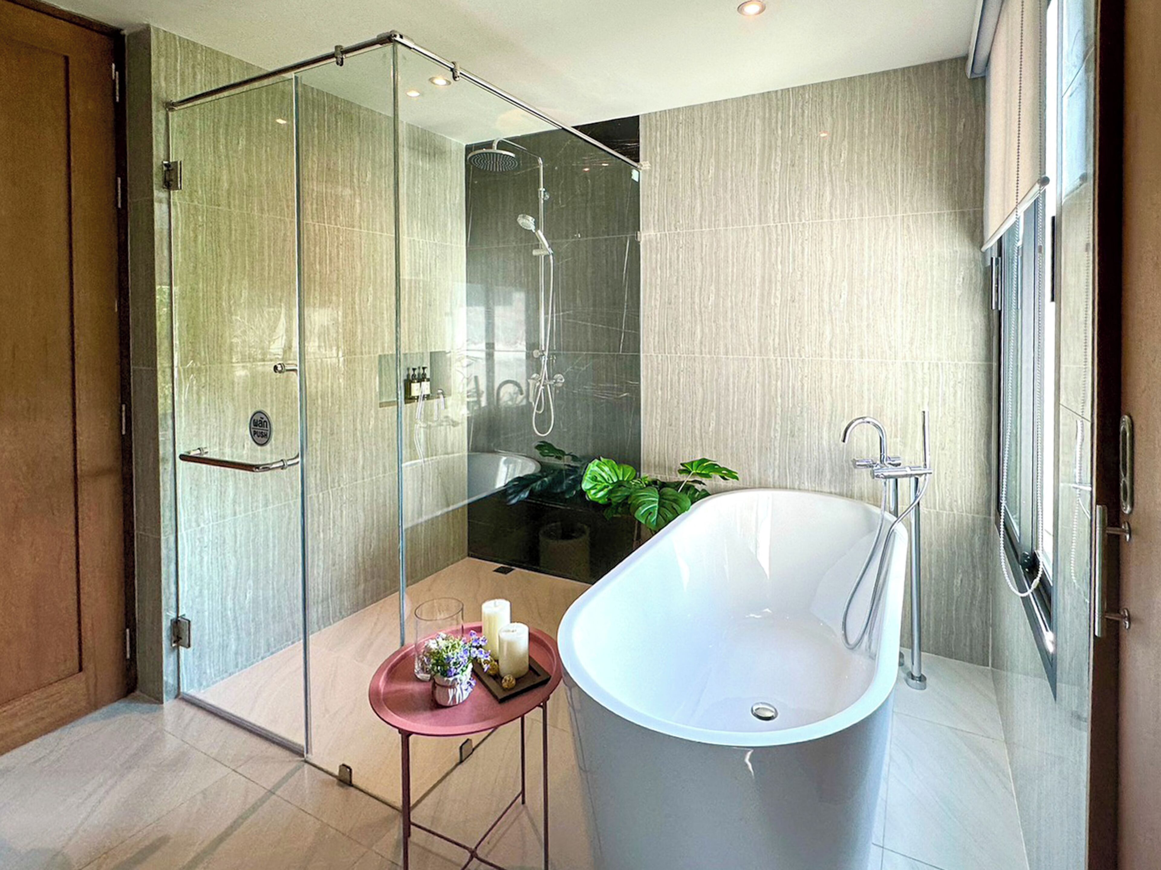 Une salle de bain moderne avec une douche à parois de verre, une baignoire sur pieds et une petite table avec des bougies.