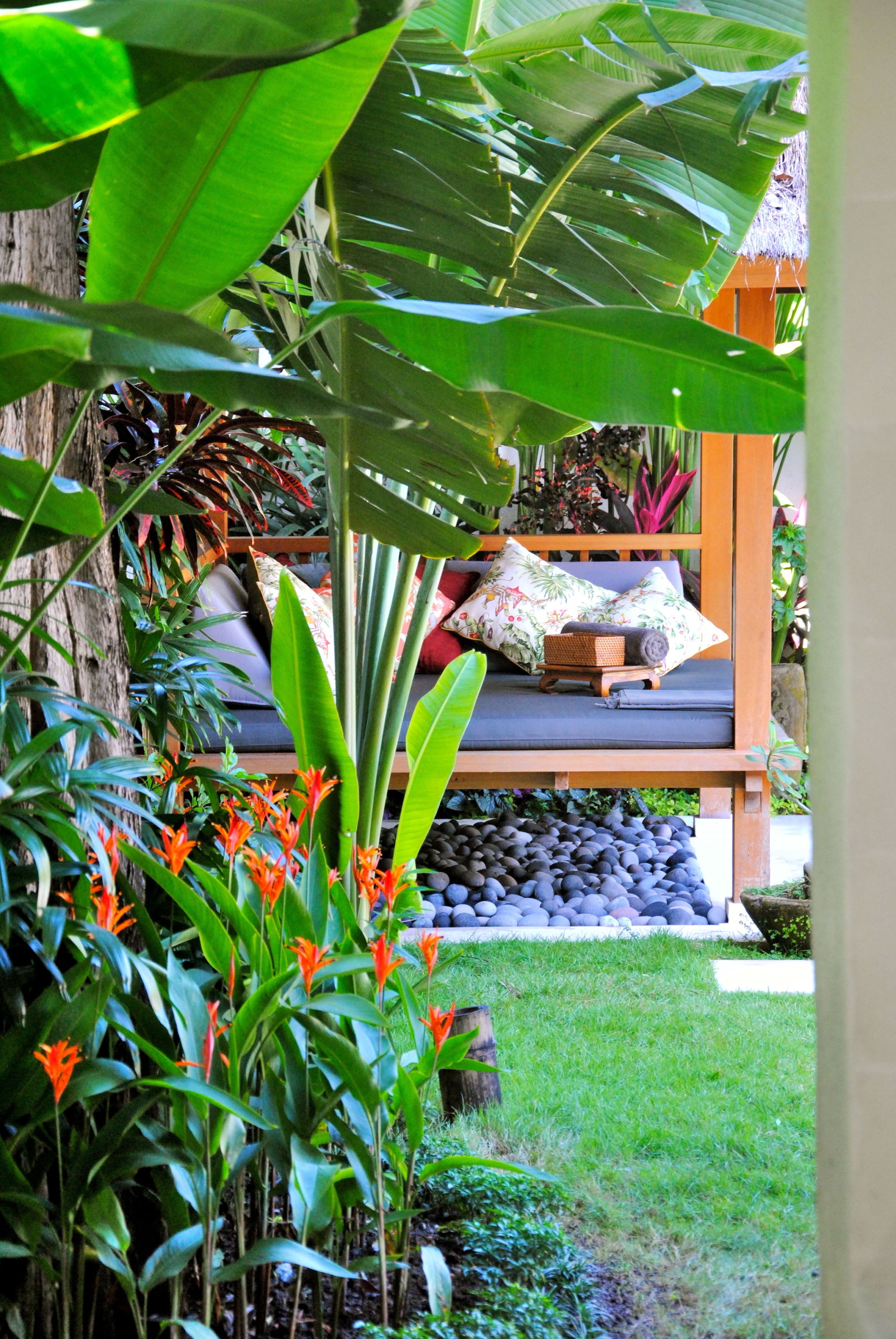 A garden with a wooden bench, tropical plants, and a stone wall.