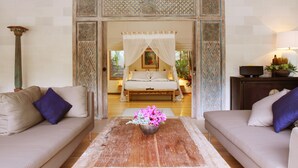 A room with a bed, two sofas, a coffee table with flowers, and a decorative archway. - Villa Bali Asri Batubelig (Seminyak)