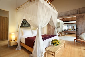 A bedroom with a four-poster bed, a bedside table with a lamp, a wooden bench, and a vase of flowers. - Villa Bali Asri Batubelig (Seminyak)