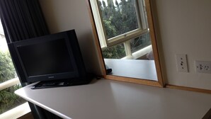 A room with a white desk, a black monitor, a window with a view of trees, and a power outlet on the wall. - Aberdeen Motor Inn (Newtown)