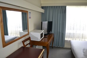 Une chambre d’hôtel avec un lit, un bureau doté d’un micro-ondes, une télévision et une fenêtre avec des rideaux.