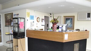 A reception desk with a black and wooden design, a vase with flowers, a clock, and a framed picture on the wall. - Aberdeen Motor Inn (Newtown)