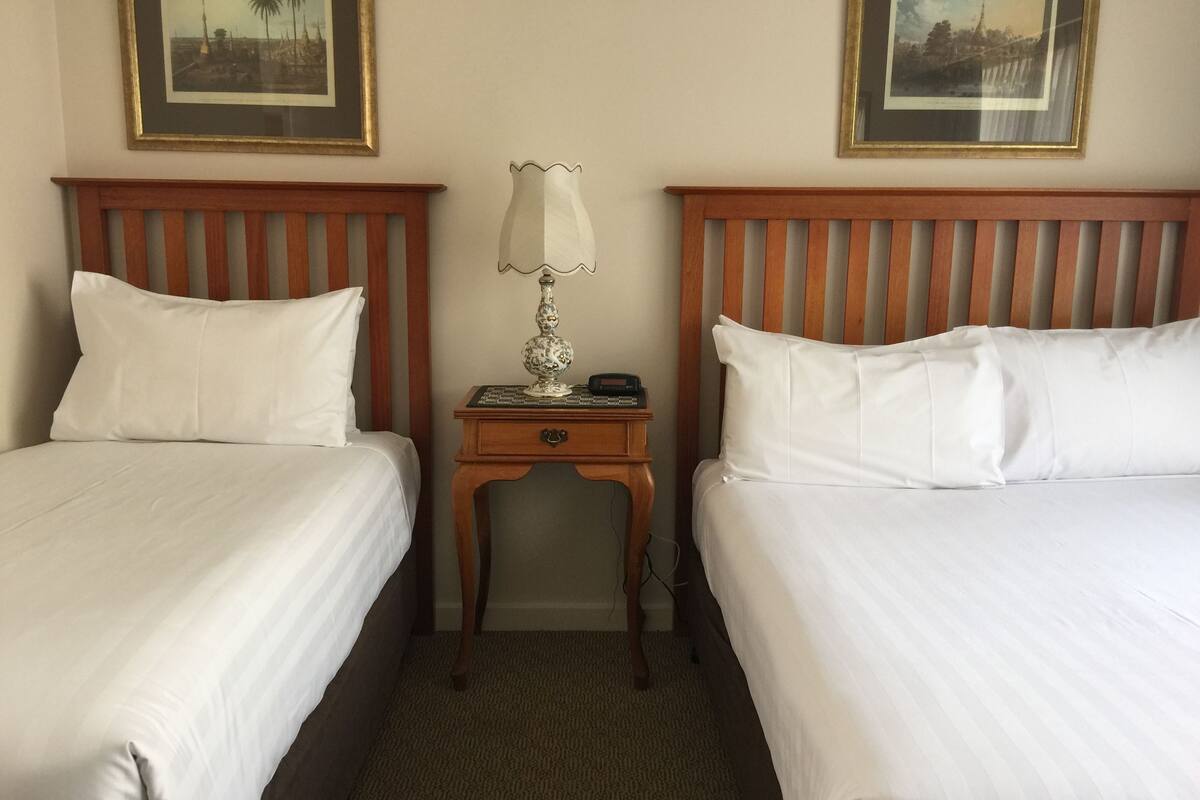 A hotel room with two single beds, a nightstand with a lamp, and framed pictures on the wall.