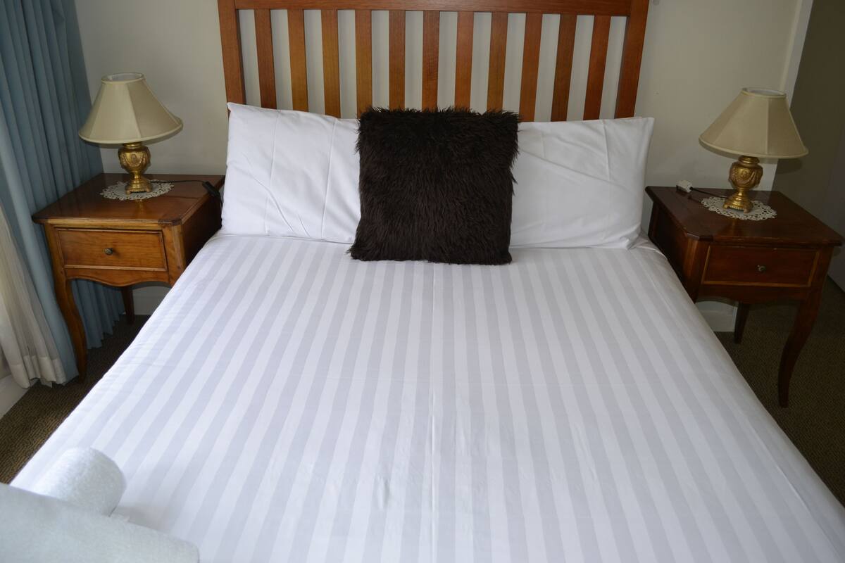 A bed with striped bedding, a black fluffy pillow, two bedside tables with lamps, and a wooden headboard.