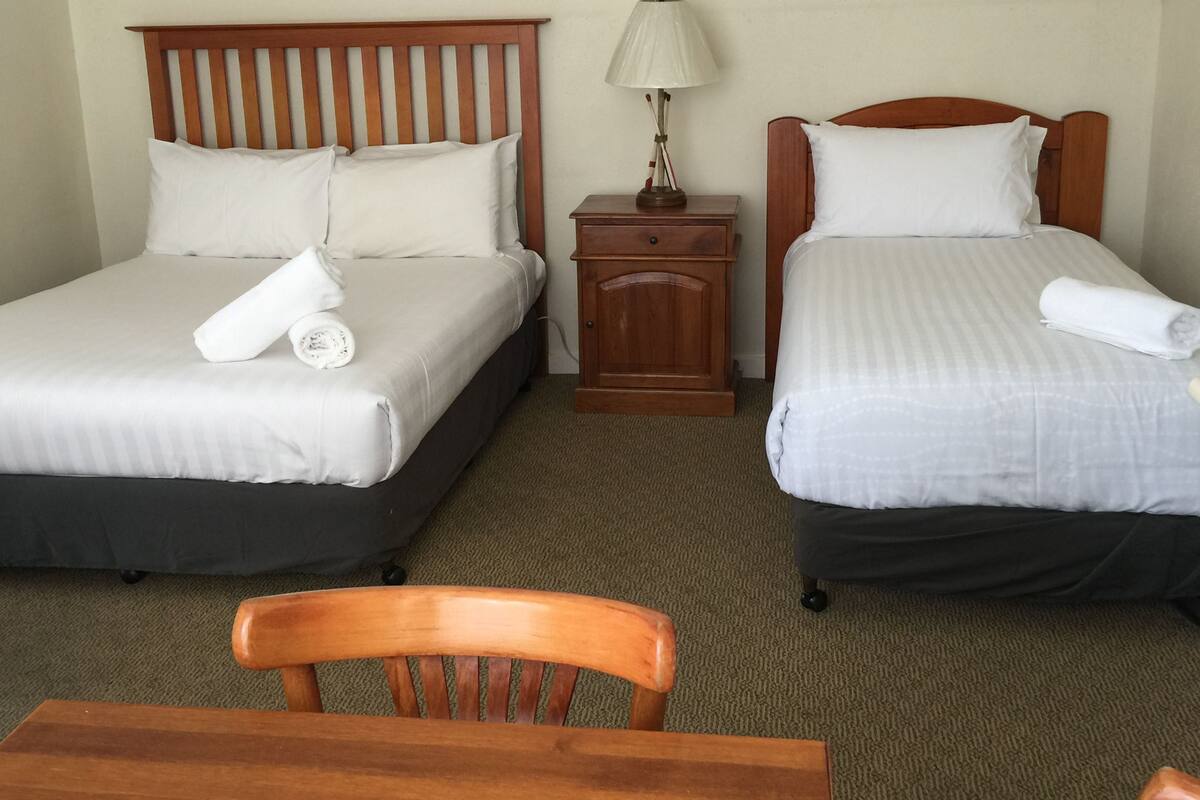 A hotel room with two beds, a wooden nightstand with a lamp, and a wooden chair.