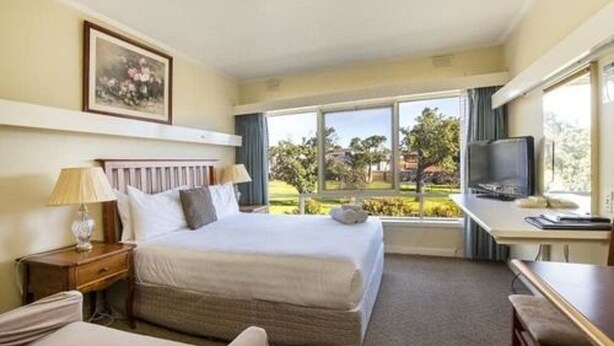 A hotel room with a bed, a desk, a television, and a window with a view of greenery. - Aberdeen Motor Inn (Newtown)