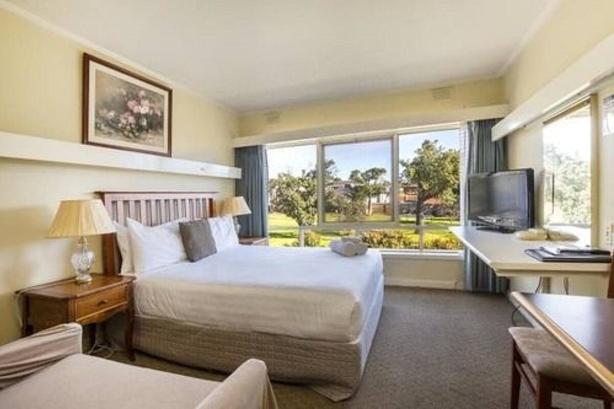 A hotel room with a bed, a desk, a television, and a window with a view of greenery.